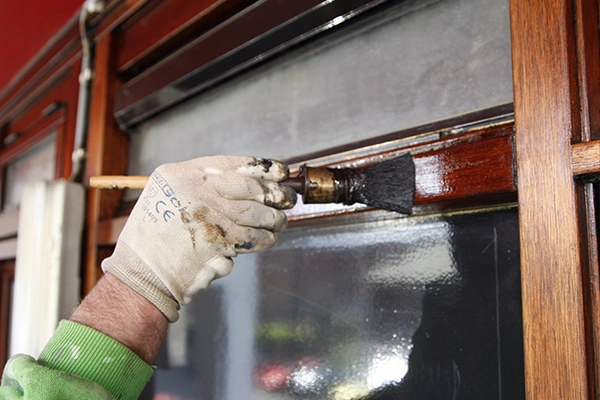 Schilder van Hemubo schildert met kwast een houten kozijn van woningbouw
